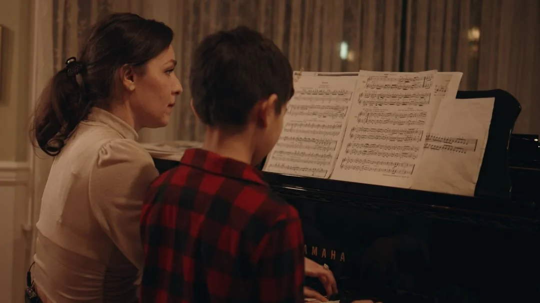 A teacher and young student reading music together at a Yamaha piano