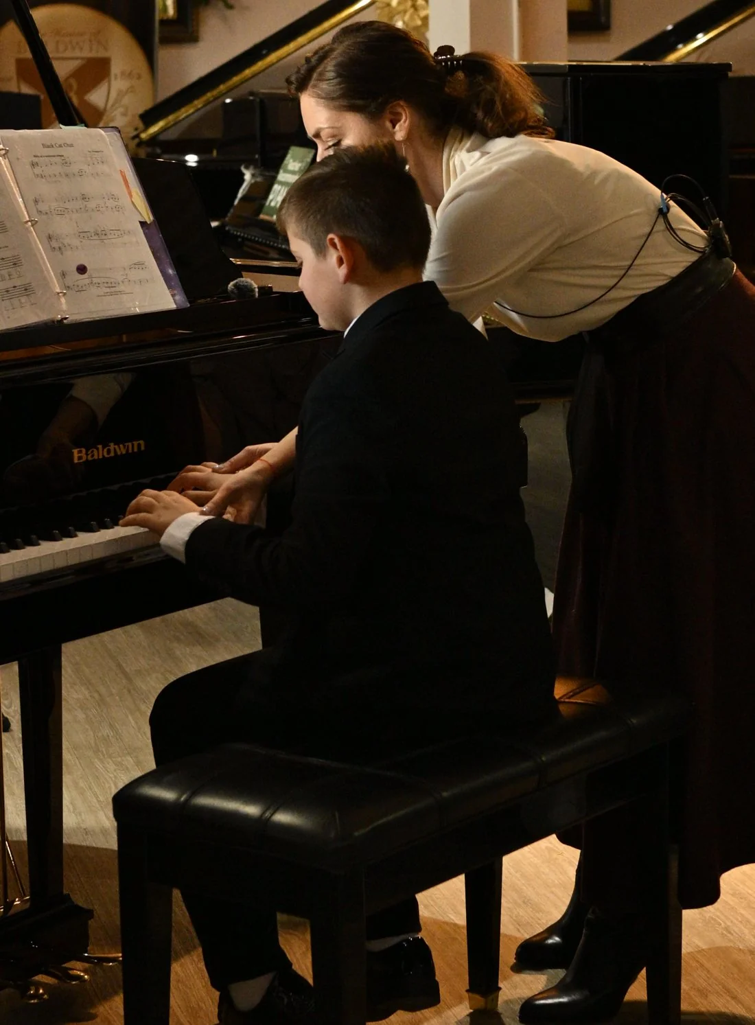 A teacher guiding a student at a Baldwin grand in the gallery